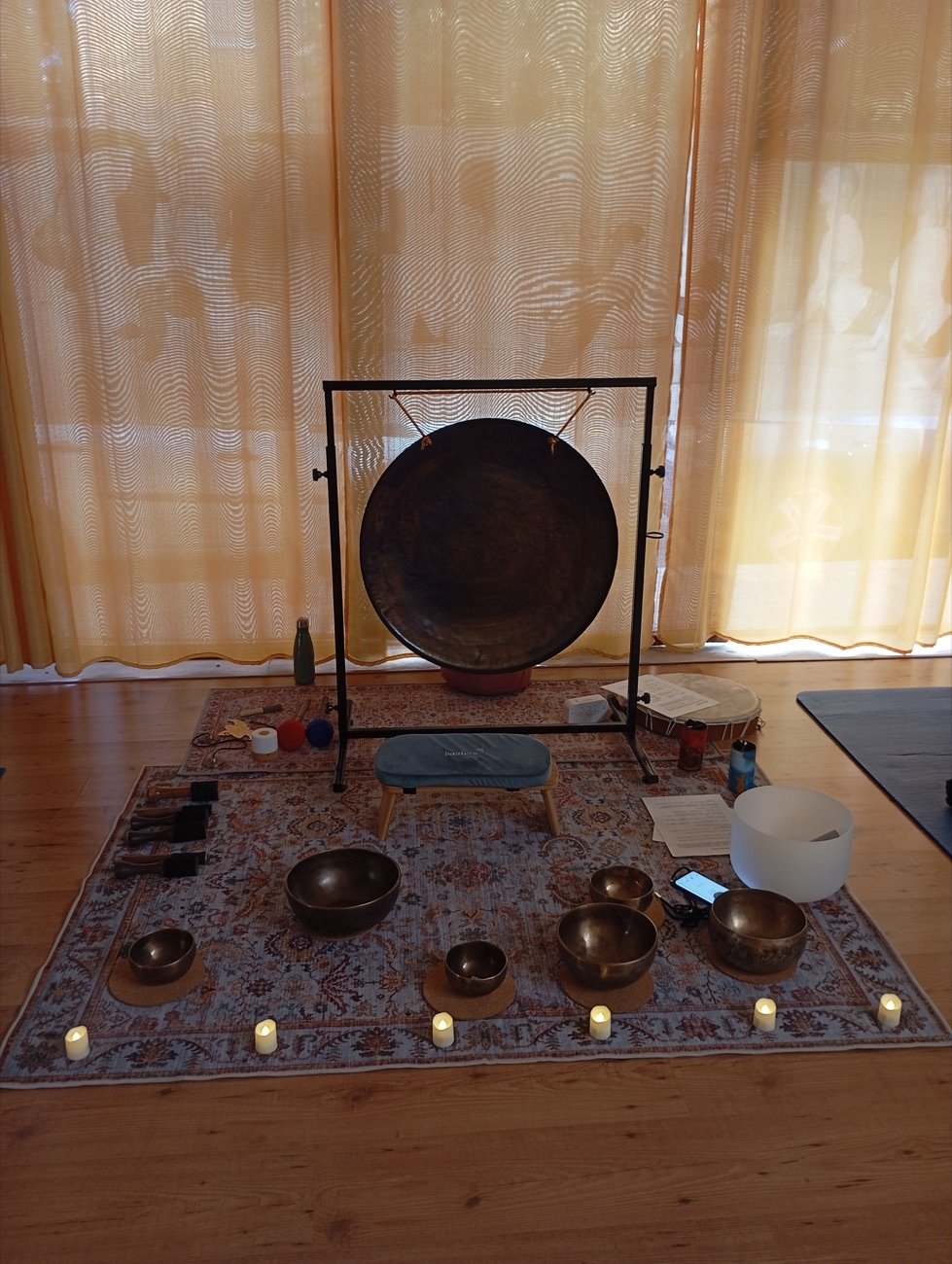 Set de baño de sonido preparado: gong, cuencos tibetanos, cuenco de cuarzo y velas sobre una alfombra.
