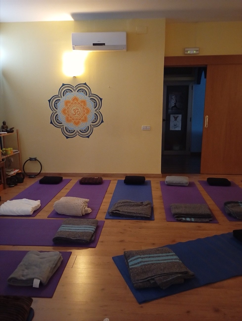 Sala preparada con esterillas, mantas y un mandala Om en la pared, lista para una sesión grupal.